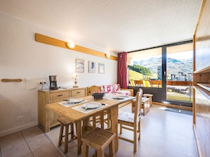 A dining area with a wooden table, chairs, and a view of mountains through a large window. - Bright studio with balcony, Ski-in/Ski-out, 4 pers (Les Menuires)