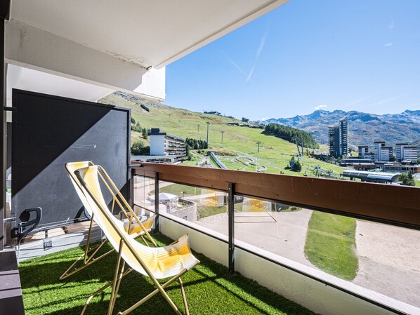 A balcony with two yellow chairs, a view of a mountainous landscape, and a building in the distance.