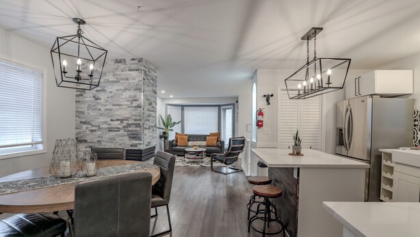 A modern kitchen with white cabinets, a stainless steel refrigerator, and a dining area with a wooden table and chairs. - Perfect Home Next To River Pathways & Downtown | 5+ Bedrooms and office (Calgary)