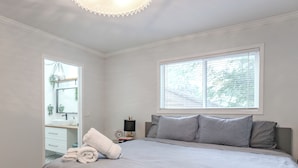 A bedroom with a bed, a window, a TV, and a bathroom visible through an open door. - Perfect Home Next To River Pathways & Downtown | 5+ Bedrooms and office (Calgary)
