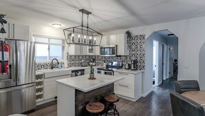 A modern kitchen with stainless steel appliances, a central island with stools, and patterned backsplash. - Perfect Home Next To River Pathways & Downtown | 5+ Bedrooms and office (Calgary)