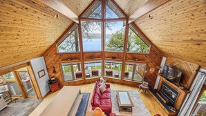 Une pièce spacieuse de style loft, avec un grand plafond en bois, une cheminée, une télévision et une vue sur l’extérieur.