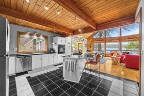 Una cocina moderna con una isla central, un comedor con sofá rojo y ventanas amplias con vistas.