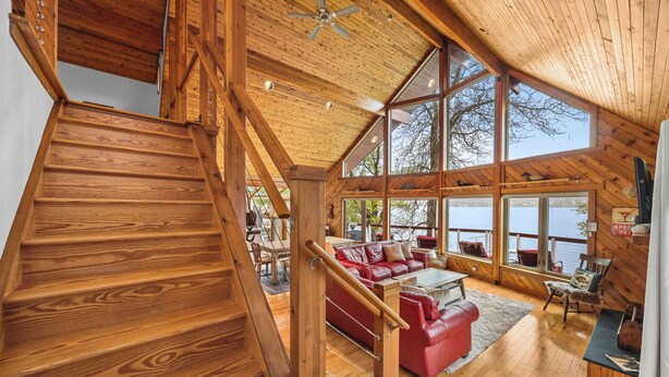 Un escalier en bois mène à une mezzanine où se trouve un canapé en cuir rouge et d’où l’on peut admirer la vue sur l’extérieur.