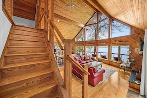 Un escalier en bois mène à une mezzanine où se trouve un canapé en cuir rouge et d’où l’on peut admirer la vue sur l’extérieur.