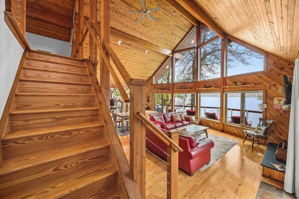A wooden staircase leading to a loft area with a red leather sofa and a view of the outdoors. - Sunset Chalet: Perfect Private Getaway! (Honeoye)