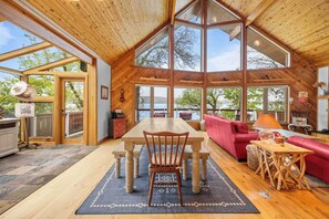 A spacious room with a wooden dining table, a red sofa, and large windows offering a view of the outdoors. - Sunset Chalet: Perfect Private Getaway! (Honeoye)