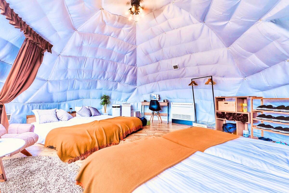 Ein Zelt-Schlafzimmer mit einem Bett, zwei Stühlen, einem Tisch und einem Schuhregal.
