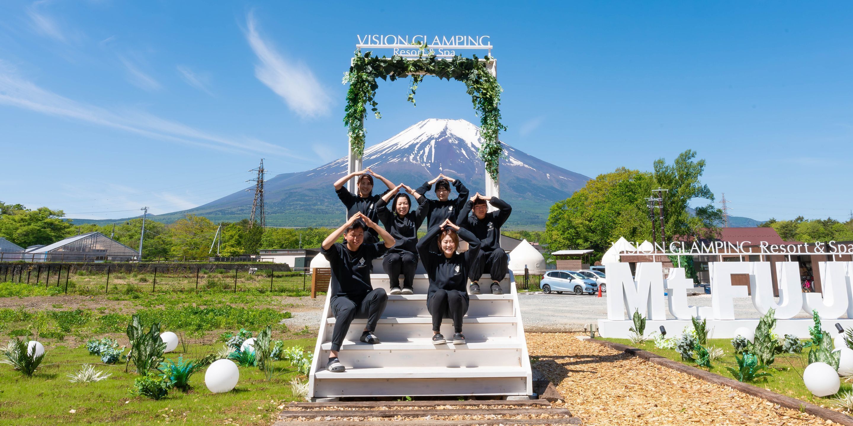 A group of people posing on a set of stairs with a sign reading "VISION CLAMPING Resort & Spa" and a mountain in the background.