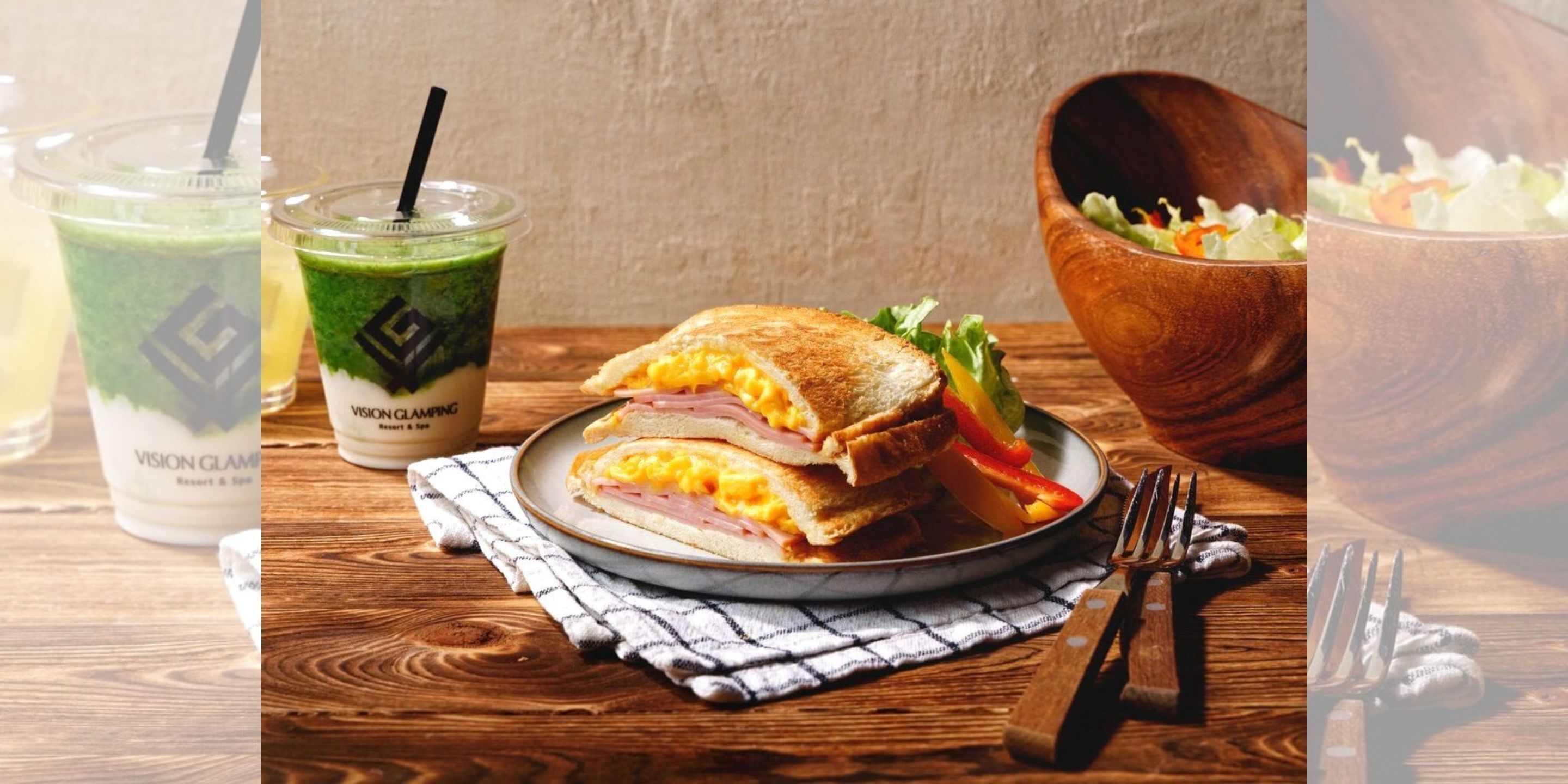 Un sándwich, una ensalada y dos bebidas sobre una mesa de madera.