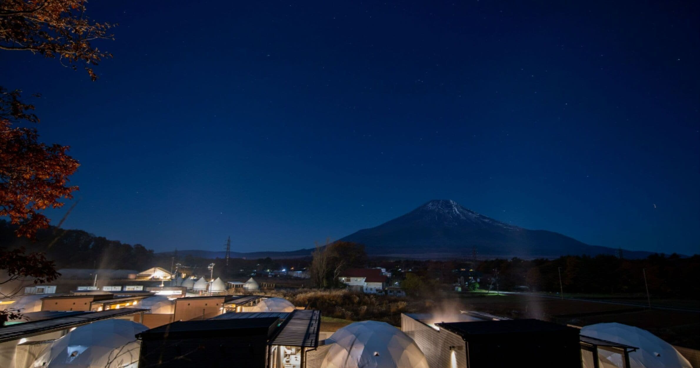 A night view of a facility with several dome-shaped structures, likely used for astronomical observations, with a prominent mountain in the background.