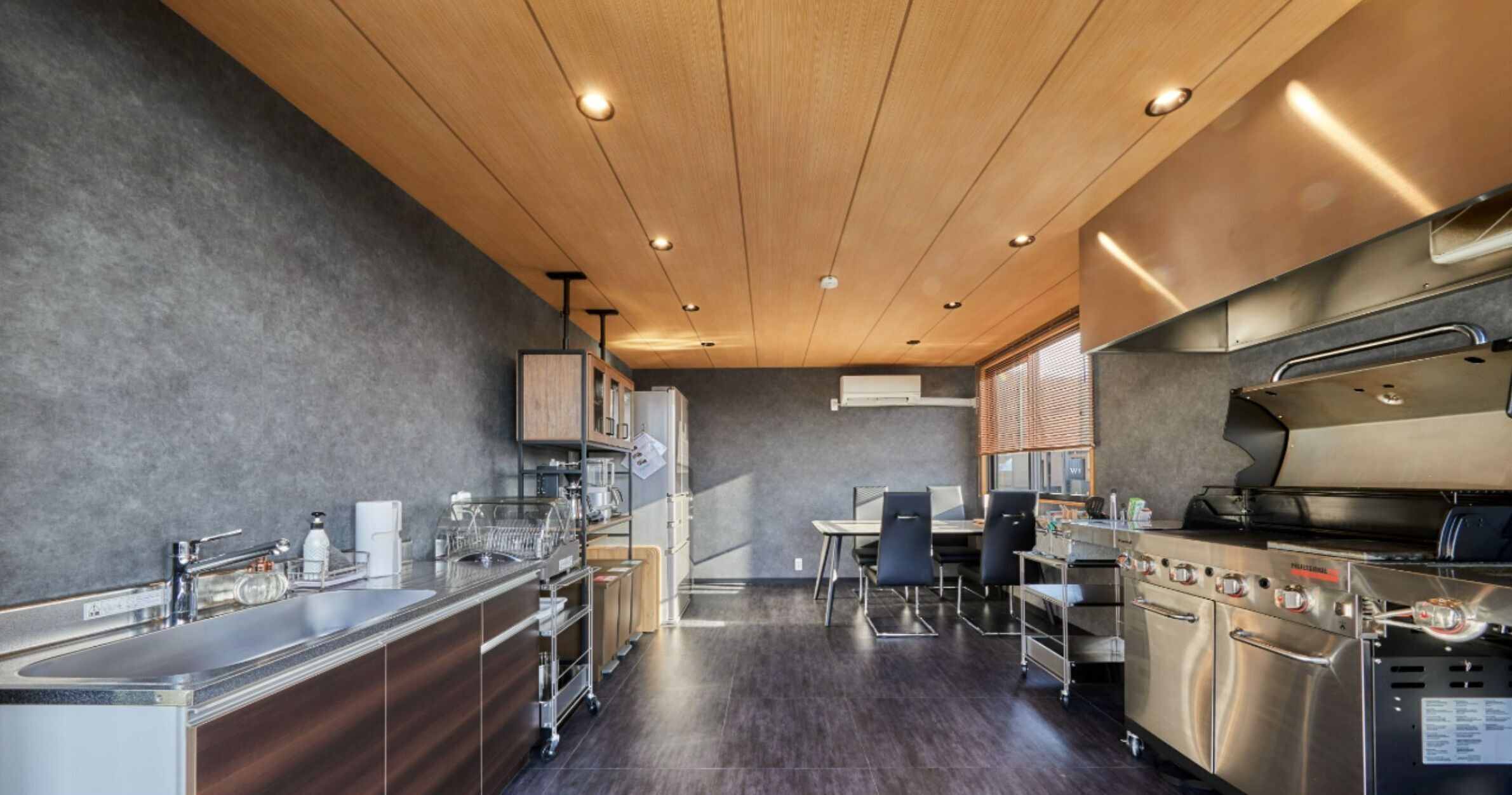 Een moderne keuken met roestvrijstalen apparatuur, een houten plafond en een eethoek met stoelen en een tafel.