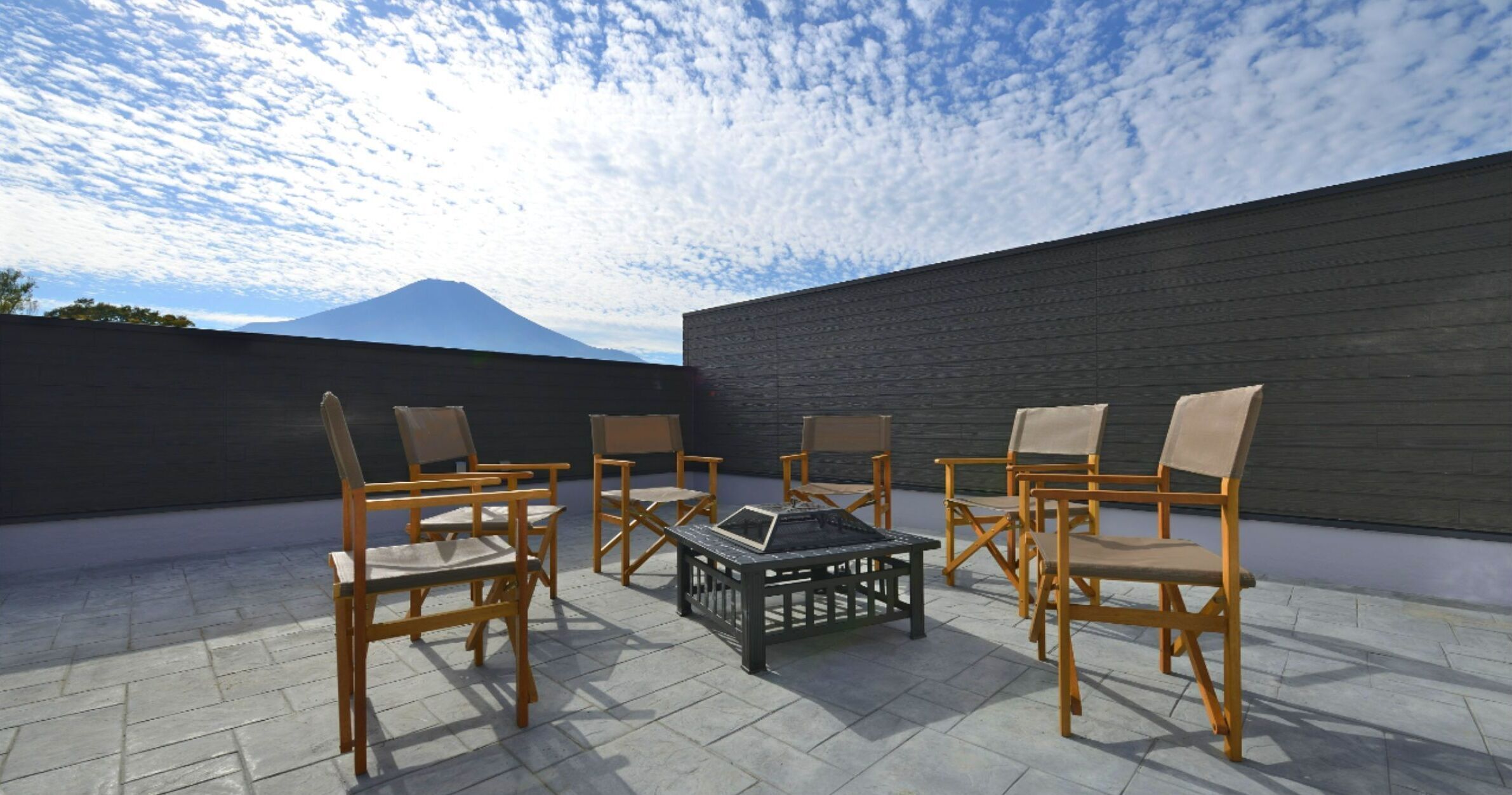 A rooftop patio with four wooden chairs and a table, a mountain in the background, and a dark wall.