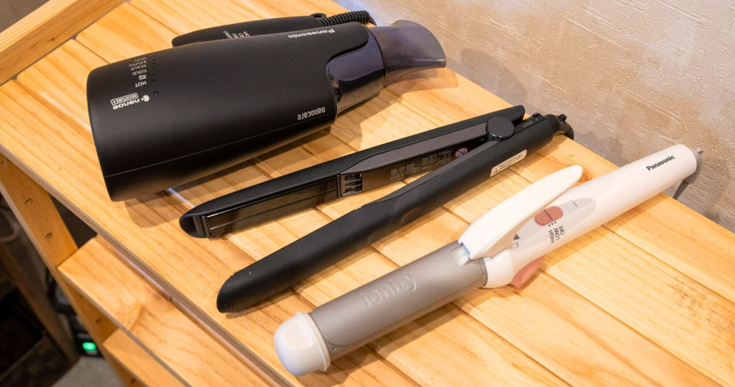 A wooden table with a hair straightener, a hair clipper, and a hairdryer.