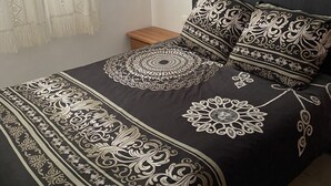 Een bed met een zwart-wit gebedruid sprei, twee kussens met vergelijkbare designs, en een houten nachtkastje naast het bed.