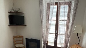 Een kleine woonkamer met een bank, een televisie, een stoel en een raam met gordijnen.