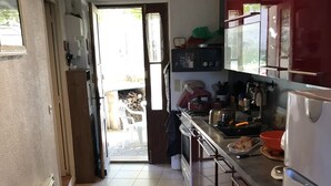 Een keuken met een fornuis, spoelbak en koelkast. Een deur leidt naar een terras.