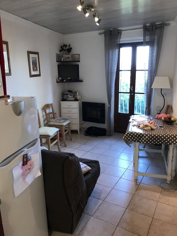 A compact living space with a kitchenette, a sofa, a dining table with a polka dot tablecloth, a TV, and a window with curtains.