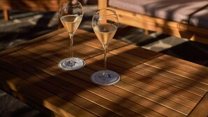 Two empty wine glasses on a wooden table in an outdoor seating area with wooden chairs and a yellow wall. - The Rif - Boutique Hotel (Pisa)