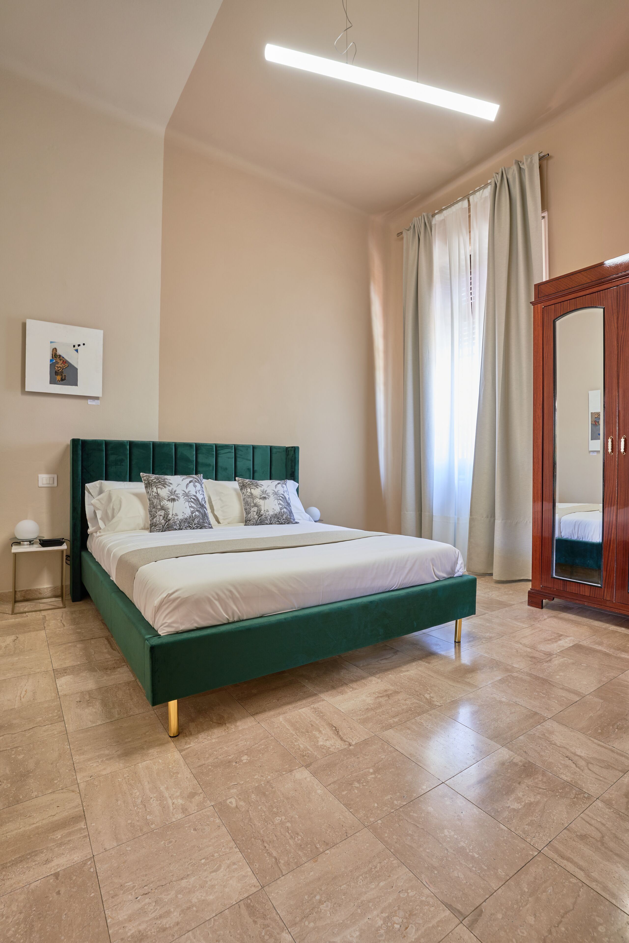 Un dormitorio con una cama tapizada en verde, un armario de madera, una mesita de noche y una lámpara en el techo.
