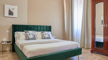 Un dormitorio con una cama tapizada en verde, un armario de madera, una mesita de noche y una lámpara en el techo.