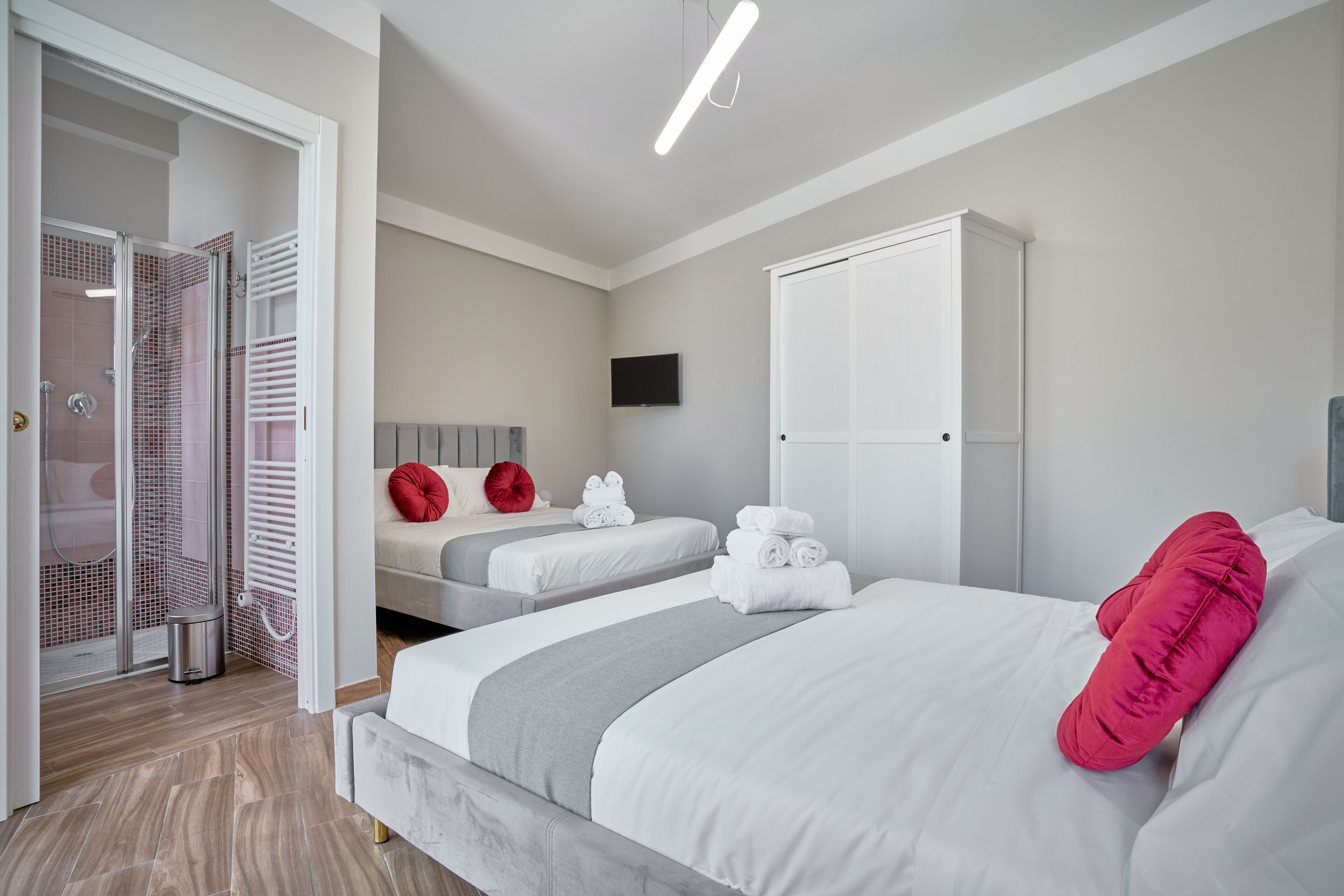 Ein modernes Hotelzimmer mit einem großen Bett, einem Einzelbett, einem begehbaren Kleiderschrank, einer Duschkabine und einem Flachbildfernseher.