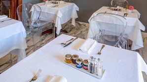 A dining area with tables set for two, clear chairs, and a variety of framed pictures on the walls. - The Rif - Boutique Hotel (Pisa)