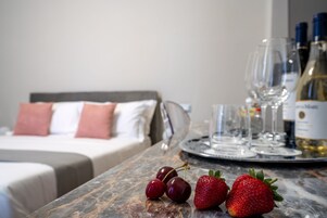 A marble table with a tray holding wine glasses and bottles, a bed with pillows, and fresh strawberries and cherries.