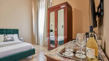 Une chambre d’hôtel avec un lit, une armoire en bois, une table en marbre avec une bouteille de vin et des verres, et un plateau.