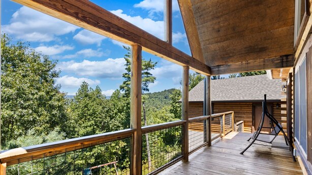 Um deck de madeira com guarda-corpo, com vista para uma área arborizada e uma montanha.
