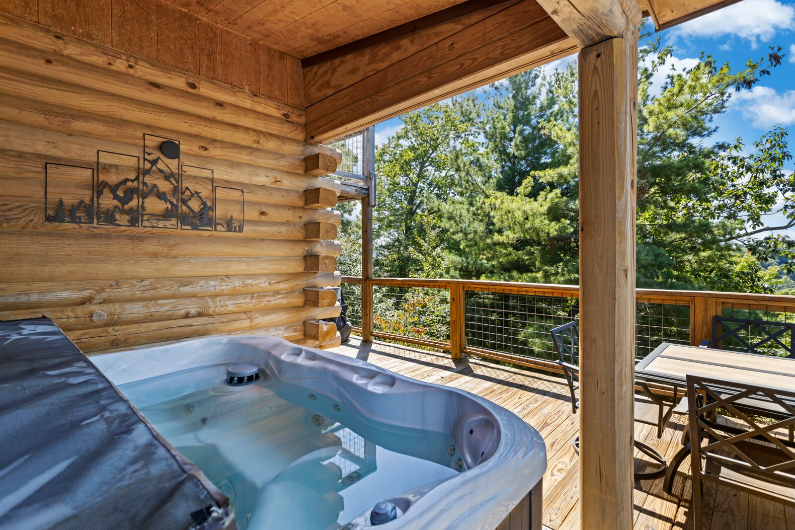 A wooden cabin with a hot tub on a deck, surrounded by trees.