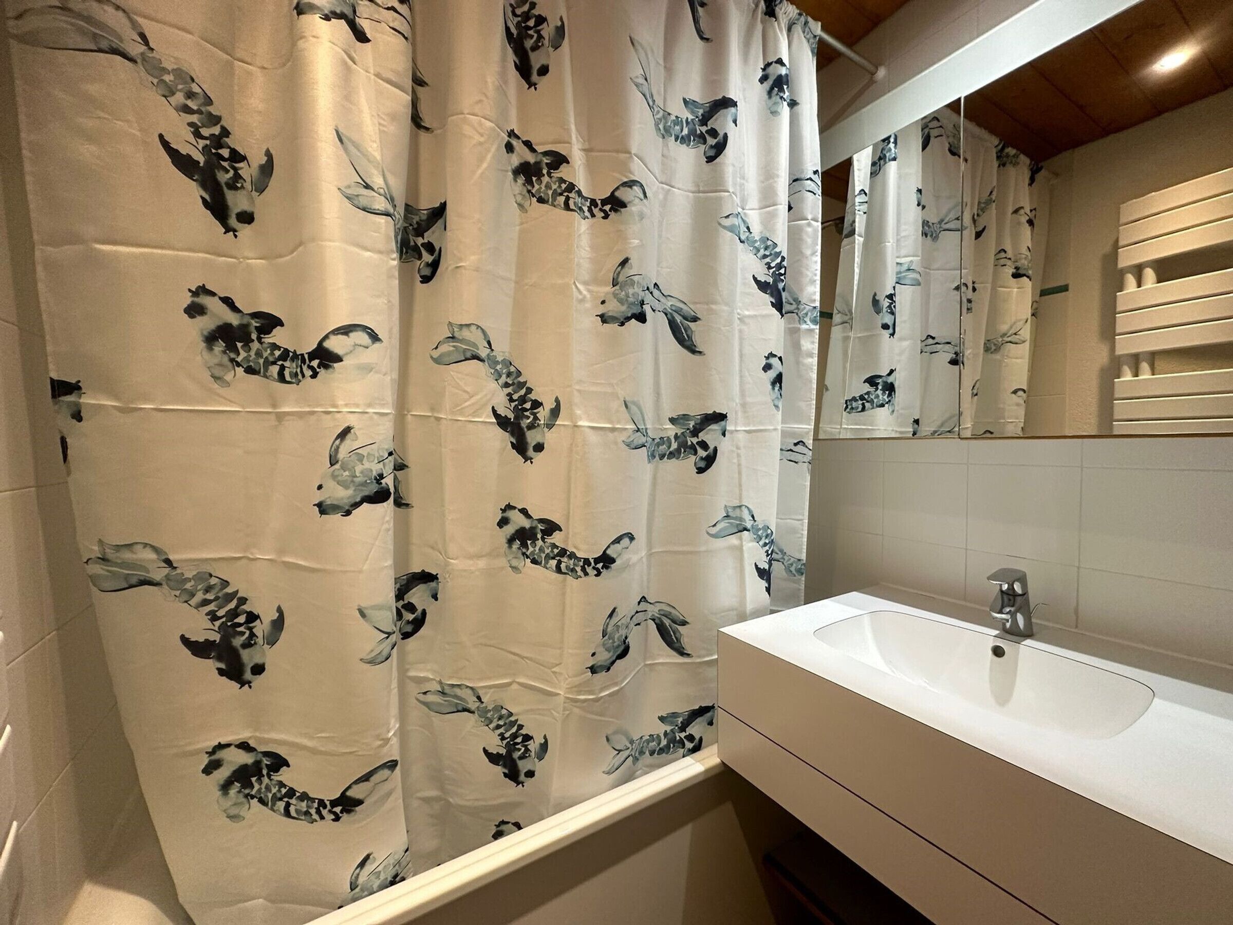 A bathroom with a white sink, a mirror, and a shower curtain with a black and white fish pattern.