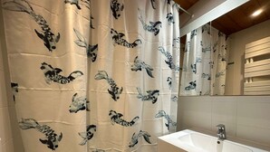 Ein Badezimmer mit einem weißen Waschbecken, einem Spiegel und einem Duschvorhang mit Fischmuster in Schwarz und Weiß.