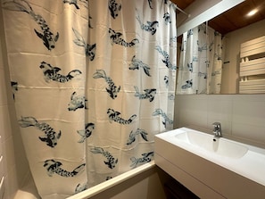 Un baño con un lavabo blanco, un espejo y una cortina de ducha con estampado de peces blanco y negro.