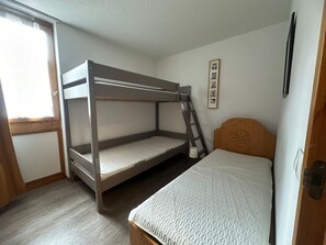 A bunk bed room with a wooden ladder, a single bed, and a small window.