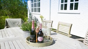 A table set outdoors with a white house in the background, featuring a bottle of champagne, a wine glass, and a tray.