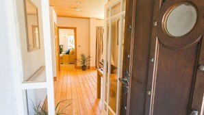A wooden door with glass panels, a hallway with wooden flooring, and a living area with a sofa and a plant.
