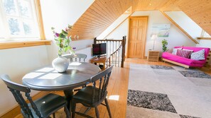 Un dormitorio loft acogedor con techo de madera, una zona de comedor con mesa y sillas, un sofá rosa y un cuadro en la pared.
