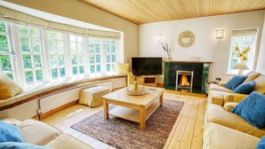 A cozy living room with a fireplace, comfortable seating, and large windows.