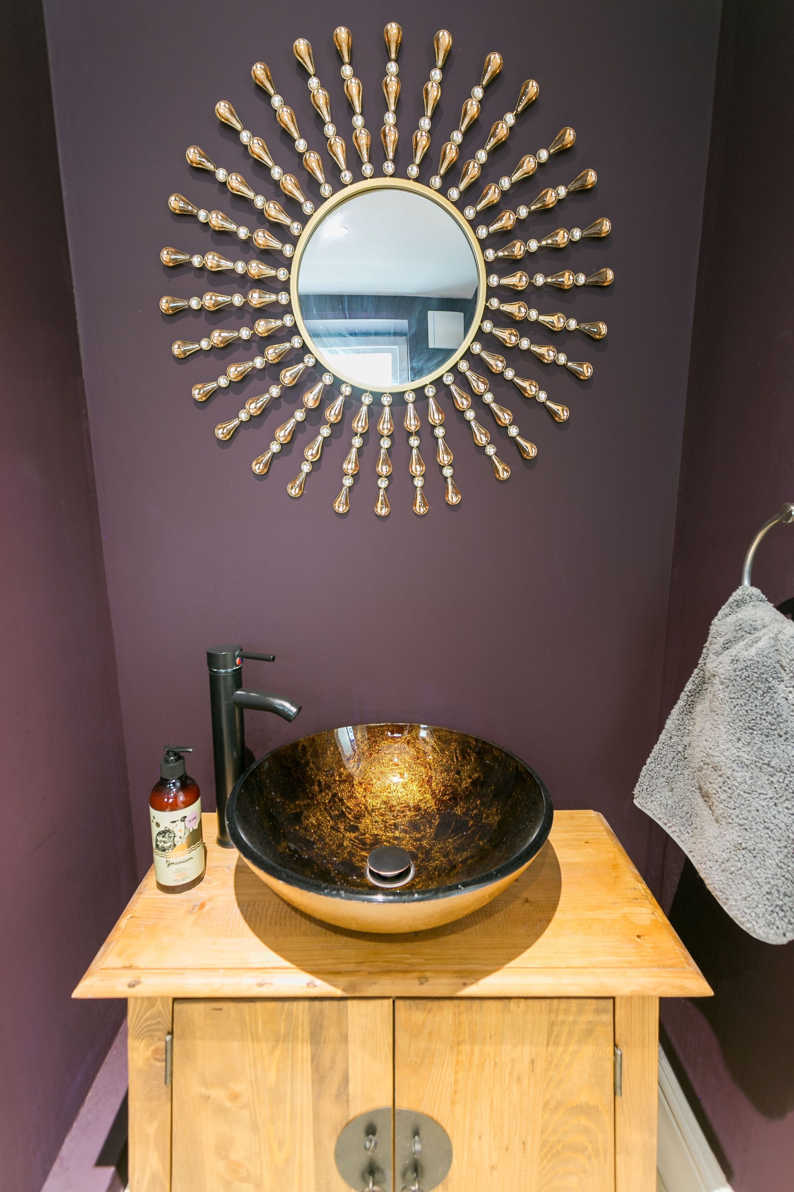 Une salle de bain avec un miroir rond, un lavabo noir, un meuble en bois et un porte-serviettes.