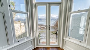 Et værelse med stor glasdør, der fører ud til en terrasse med udsigt over bjerge og et vandområde.