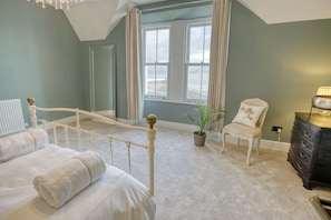 A bedroom with a bed, a chair, a dresser, a window with curtains, and a plant.