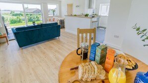 Un soggiorno moderno con un divano blu, un tavolo da pranzo in legno con cose per la colazione e una cucina sullo sfondo.