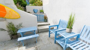 A patio with blue wooden furniture, potted plants, and a surfboard.