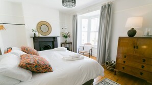 A neatly arranged bedroom with a large bed, a dresser, a chair, and a fireplace.