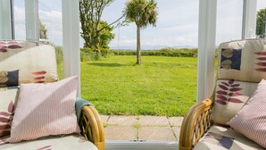 Une véranda meublée de mobilier en osier, donnant sur un jardin verdoyant agrémenté d’un palmier.