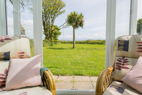 A conservatory with wicker furniture and a view of a grassy garden with a palm tree.