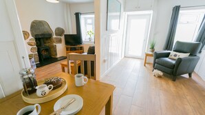Un salon chaleureux avec une cheminée en pierre, un fauteuil confortable et un coin repas avec une table en bois mise pour le repas.