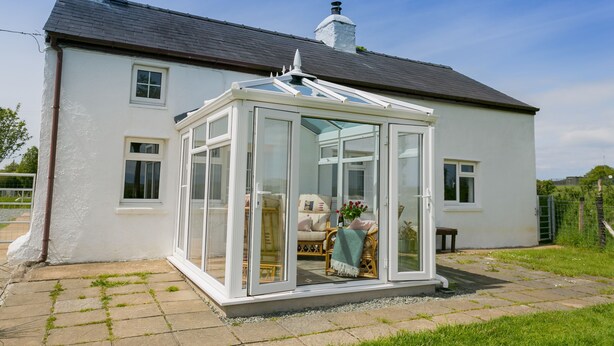 Une maison blanche avec une véranda, une cheminée et un jardin.