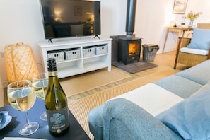 Uma sala de estar com sofá, televisão, lareira e uma garrafa de vinho sobre uma mesa.